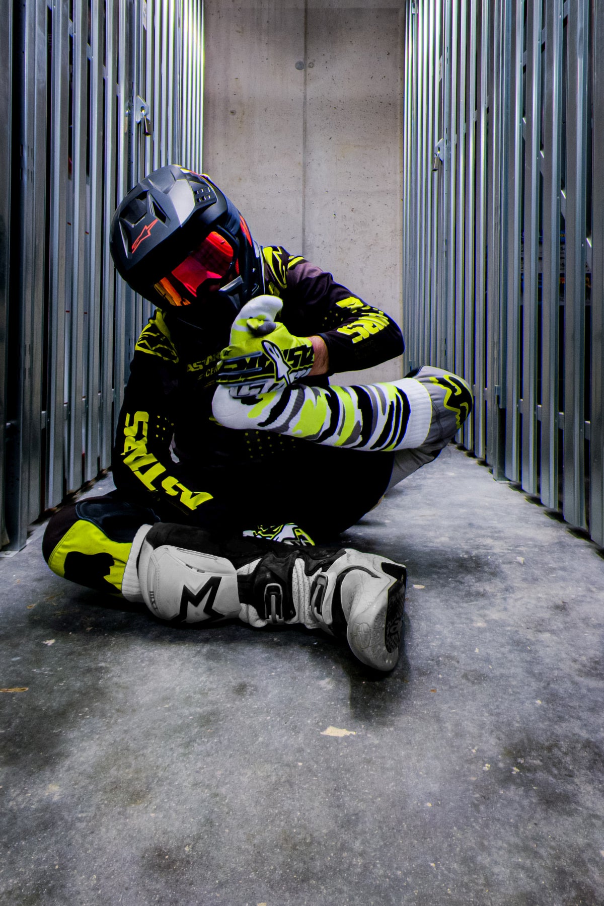 motocross biker in a neon yellow outfit with cross boots and neon yellow MX socks by sk8erboy, front view, sitting on the floor in the boots and sniffing