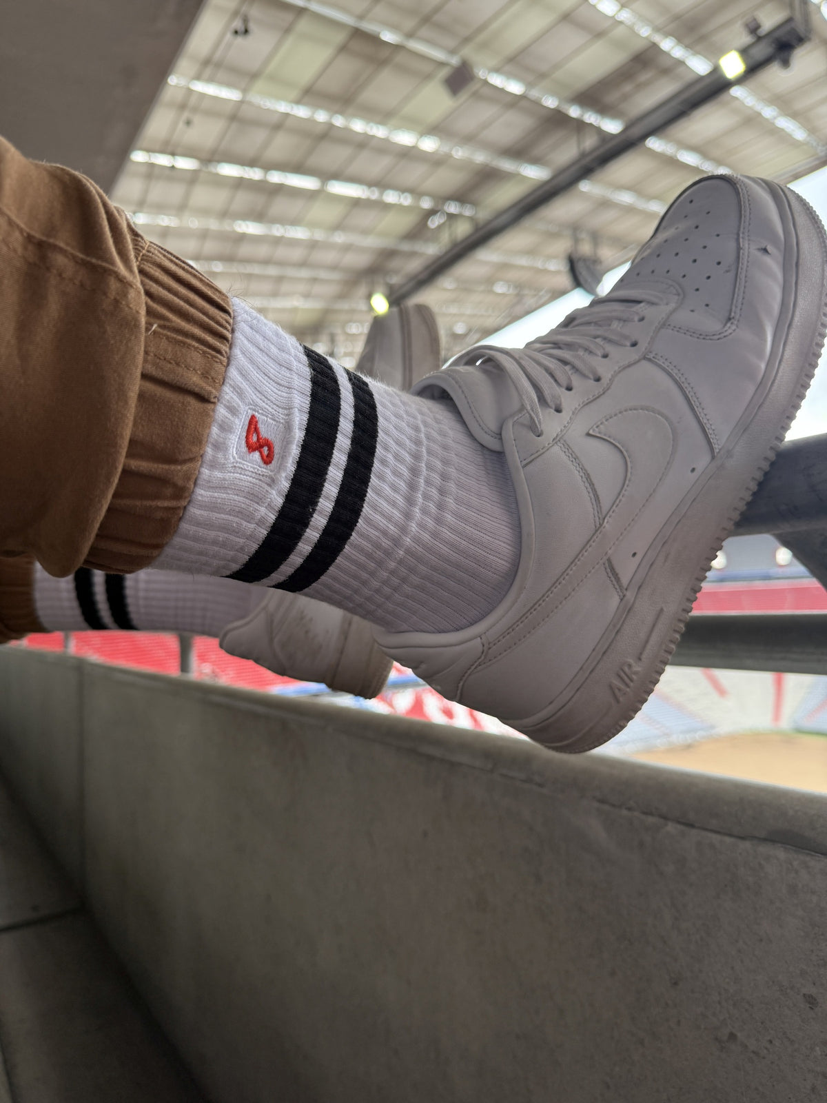 Gros plan sur des chaussettes rétro Sk8erboy® à rayures noires, portées avec des sneakers Nike blanches dans un stade – look gay sportif au fort effet statement.
