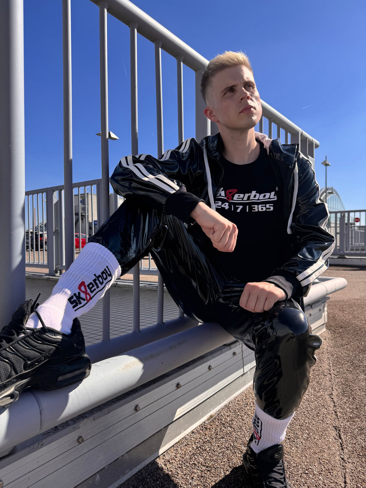 hübscher gay twink trägt ein sk8erboy t-shirt shirt in schwarz baumwolle cotton mit einem sk8erboy aufdruck mit weisser schrift und 8 acht in rot mit 24 7 365 fetter aufdruck in pvc kleidung
