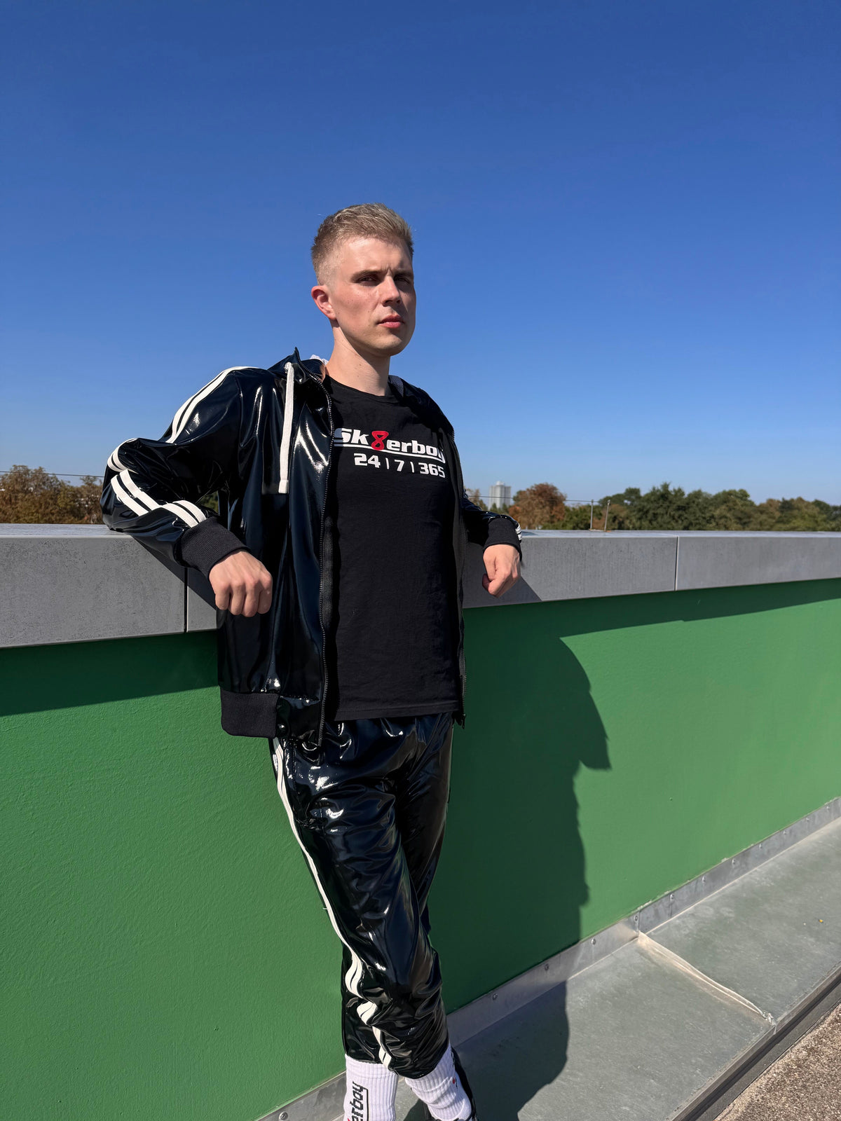 hübscher gay twink trägt ein sk8erboy t-shirt shirt in schwarz baumwolle cotton mit einem sk8erboy aufdruck mit weisser schrift und 8 acht in rot mit 24 7 365 fetter aufdruck und pvc kleidung