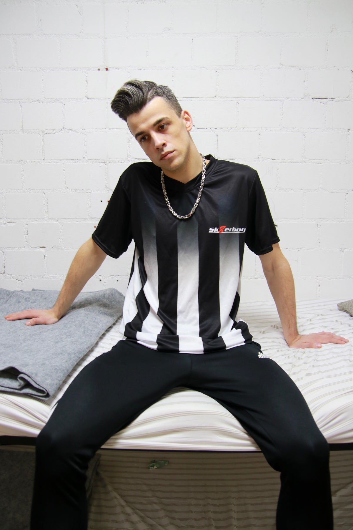 Urbaner Look: Model sitzt mit dem Sk8erboy® Tikot und glänzender Jogginghose in einem Stockbett in einer Gefängniszelle
