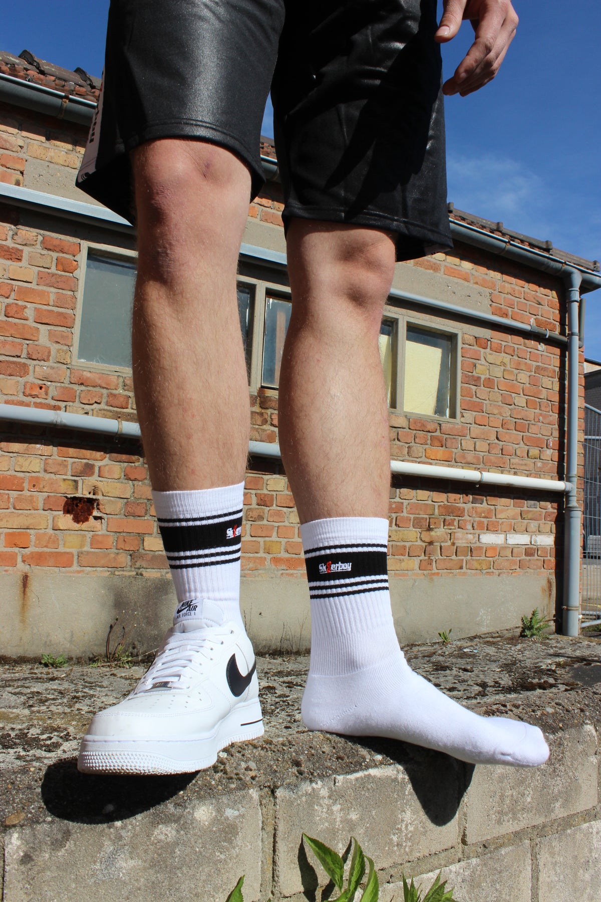 sk8erboy deluxe socken sox in weiss mit schwarzen ringen schwarzen mit schwarzem streifen und logo einstickung rote 8 acht er traegt nike afo air force one low mit weissem leder und schwarzem leder nike swoosh haken im hintergrund ein lostplace der boy hat einen blanken unterschenkel mit haaren