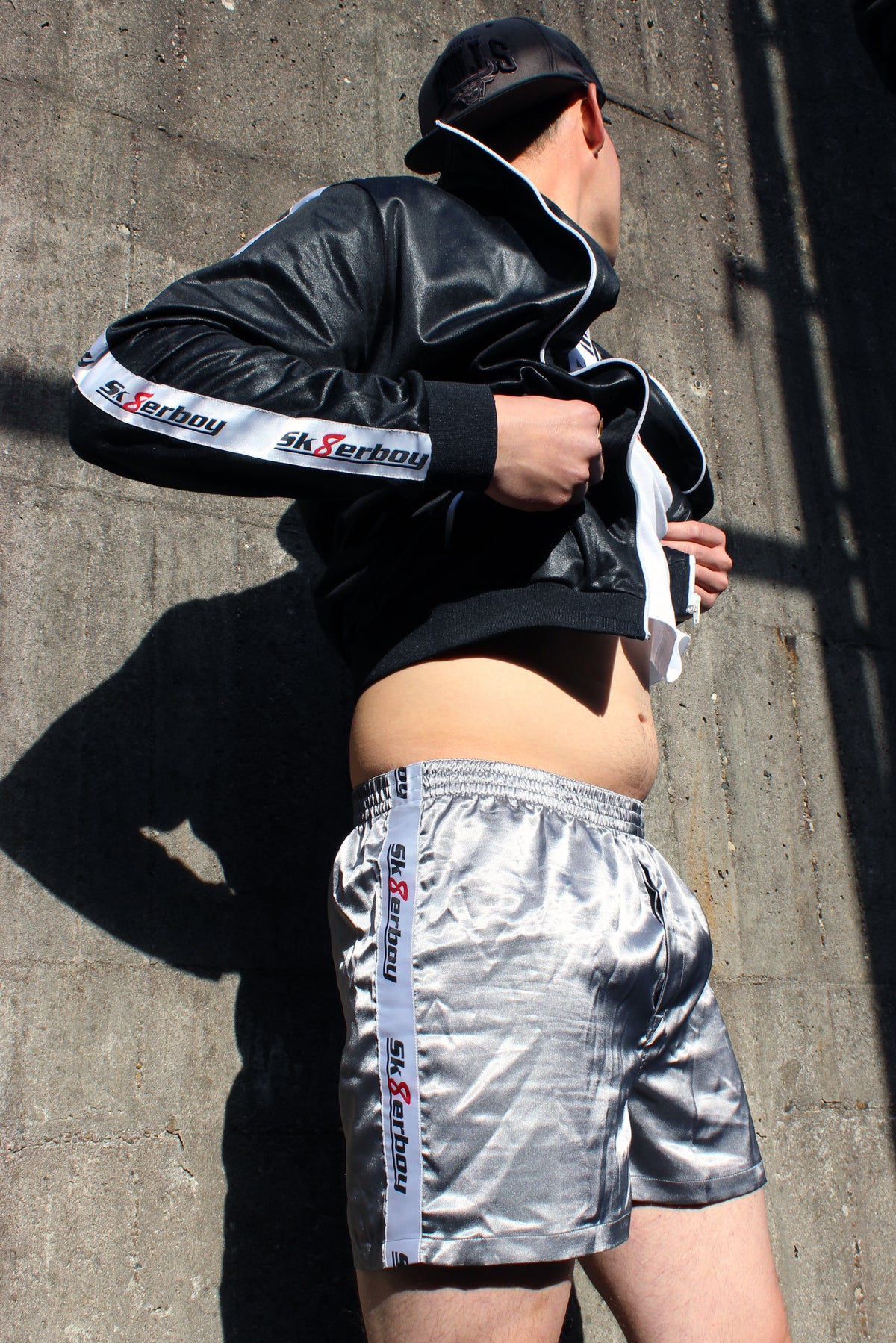 sk8erboy shiny glaenzend satin silver silber glanz boxershort brief mit fettem sk8erboy streifen in weiss mit schwarzem Schriftzug und roter acht 8 seine sexy behaarten beine enden in geilen nike Shox nz sneaker sneax von nike weiss Leder perfekt zu lecken die deluxe socks in weiss von sk8erboy mit schwarzen ringen runden das perfekt ab das logo ist gestickt mit einer roten acht der boy Bengel Kerl mann steht vor einer Backsteinwand an einem roten lostplace Fabrik weg beton Jacke wird hochgezogen