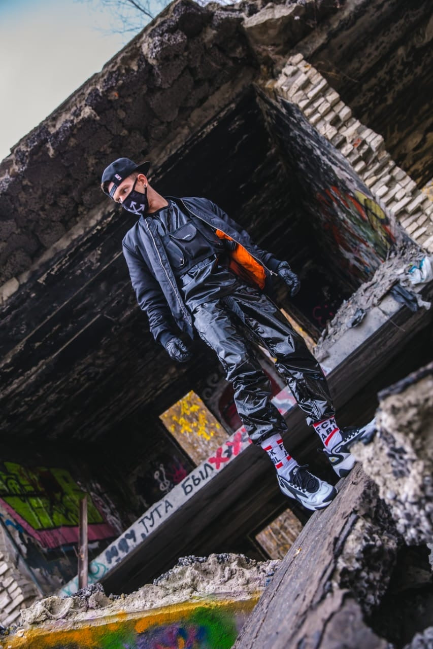 sexy gay steht auf einem verlassenen gebäude mit pvc sportanzug bomberjacke und maske dazu fck abl socks von sk8erboy und weissen nike air max sneaker