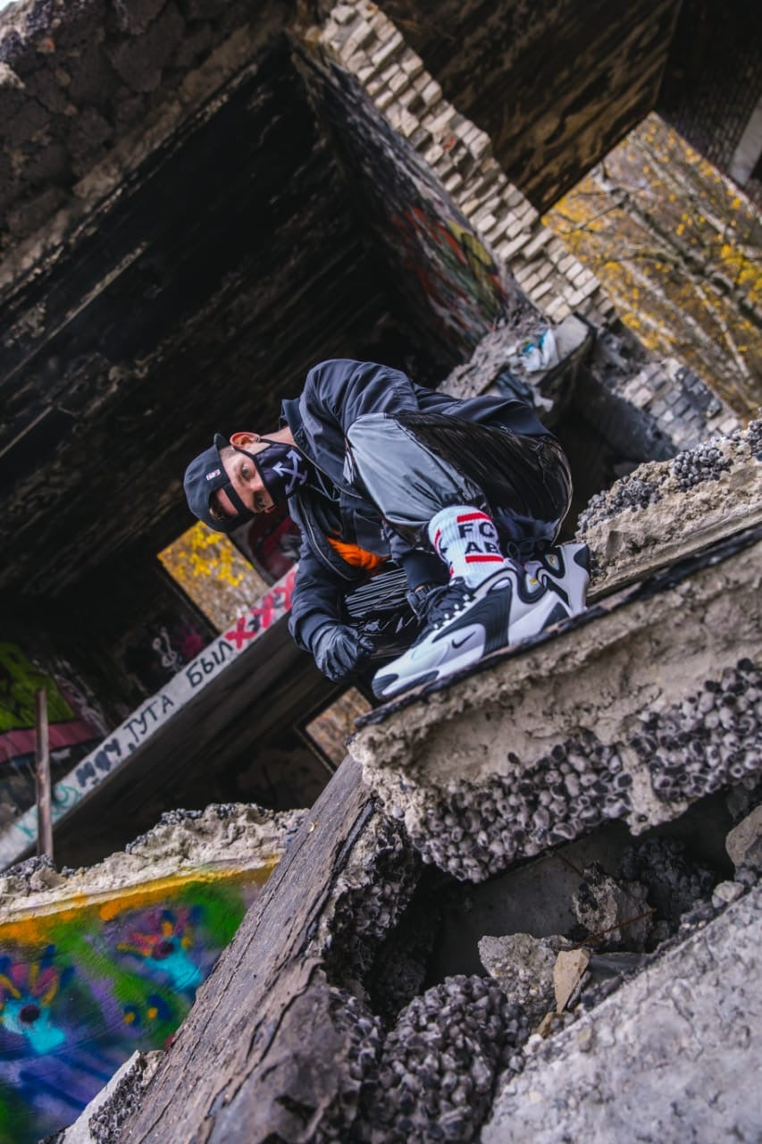 sexy gay mit maske und kappe trägt pvc sportanzug auf einem verlassenen gebaeude dazu fck abl socks von sk8erboy in seinen nike air max sneaker