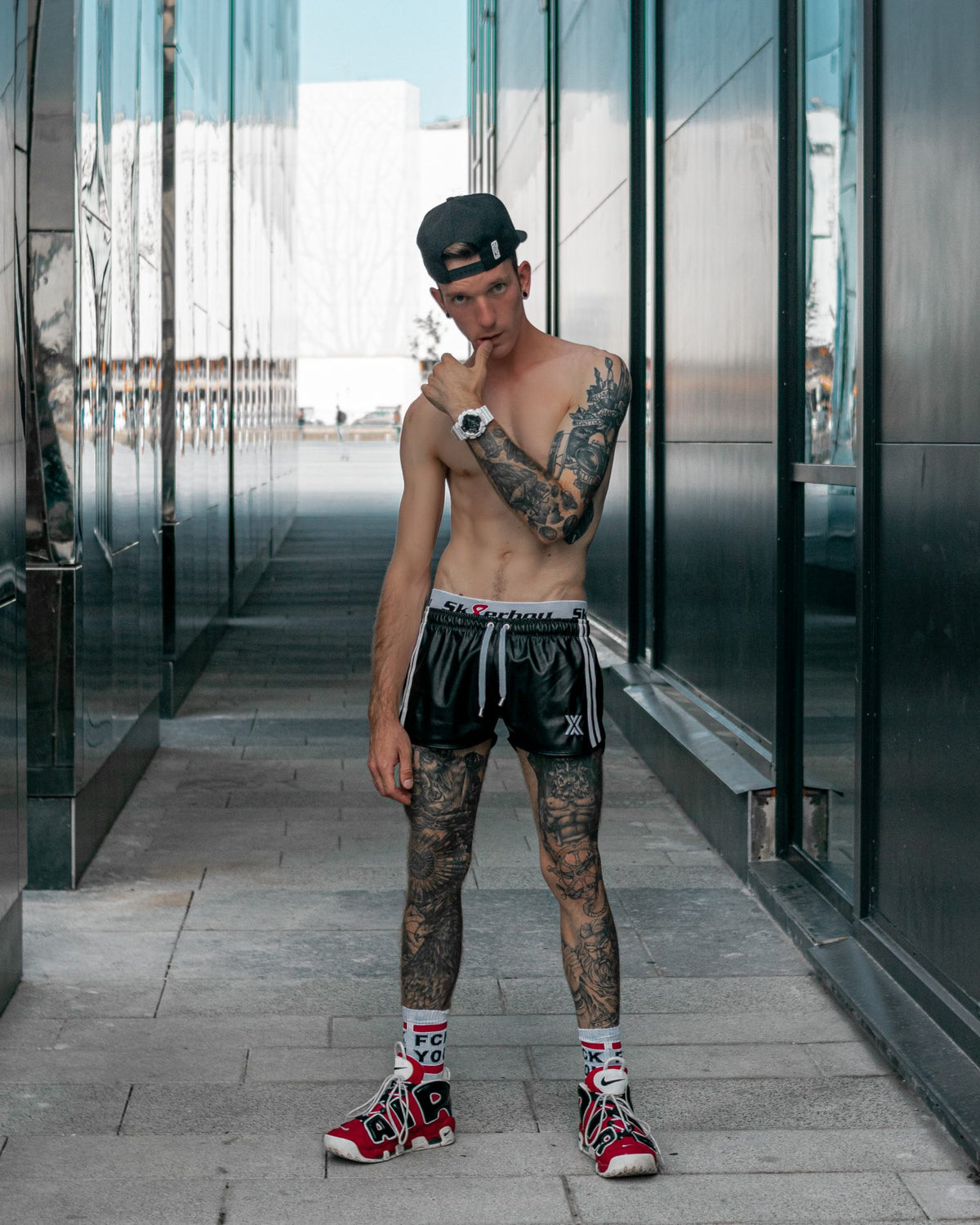 sportlicher gay in der stadt mit nacktem oberkoerper traegt eine schwarze short von boxer berlin und einen sk8erboy jock zu seinen fck you socks von sk8erboy socken mit roten nike air sneaker
