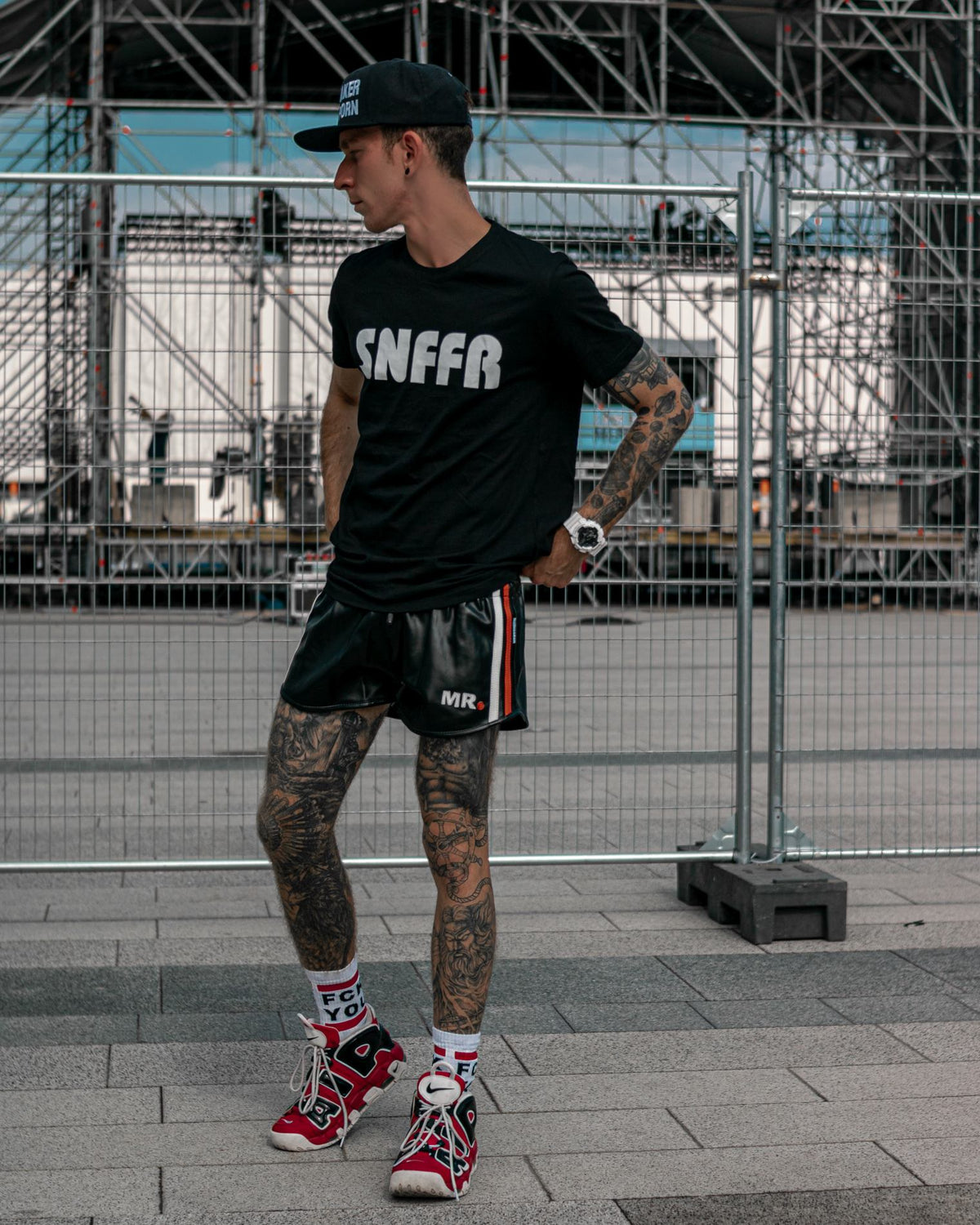 junger boy mit schwarzem snffr t-shirt und mr riegillio short aus veganem leder zu den fck you socks von sk8erboy zeigt seine tattoos