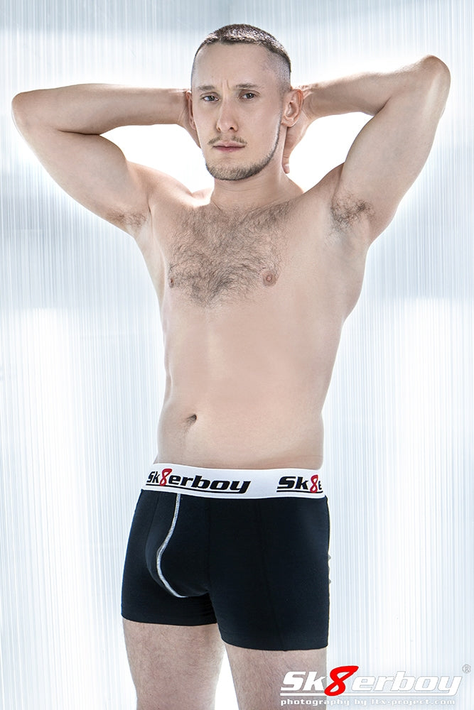 vue de côté d’un boxer noir sk8erboy avec grand logo à la taille, porté par un jeune homme mince devant un mur blanc