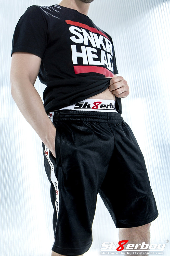 Young gay man wearing short shiny black shorts by sk8erboy with matching boxer shorts underneath and a snkr head T-shirt for summer