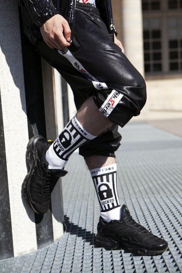 jeune gay portant des chaussettes verrouillées de sk8erboy avec cadenas à la taille et 365 24 7 à la taille pour les fans de chastity, de chasteté ou de bondage, avec pantalon brillant à Berlin