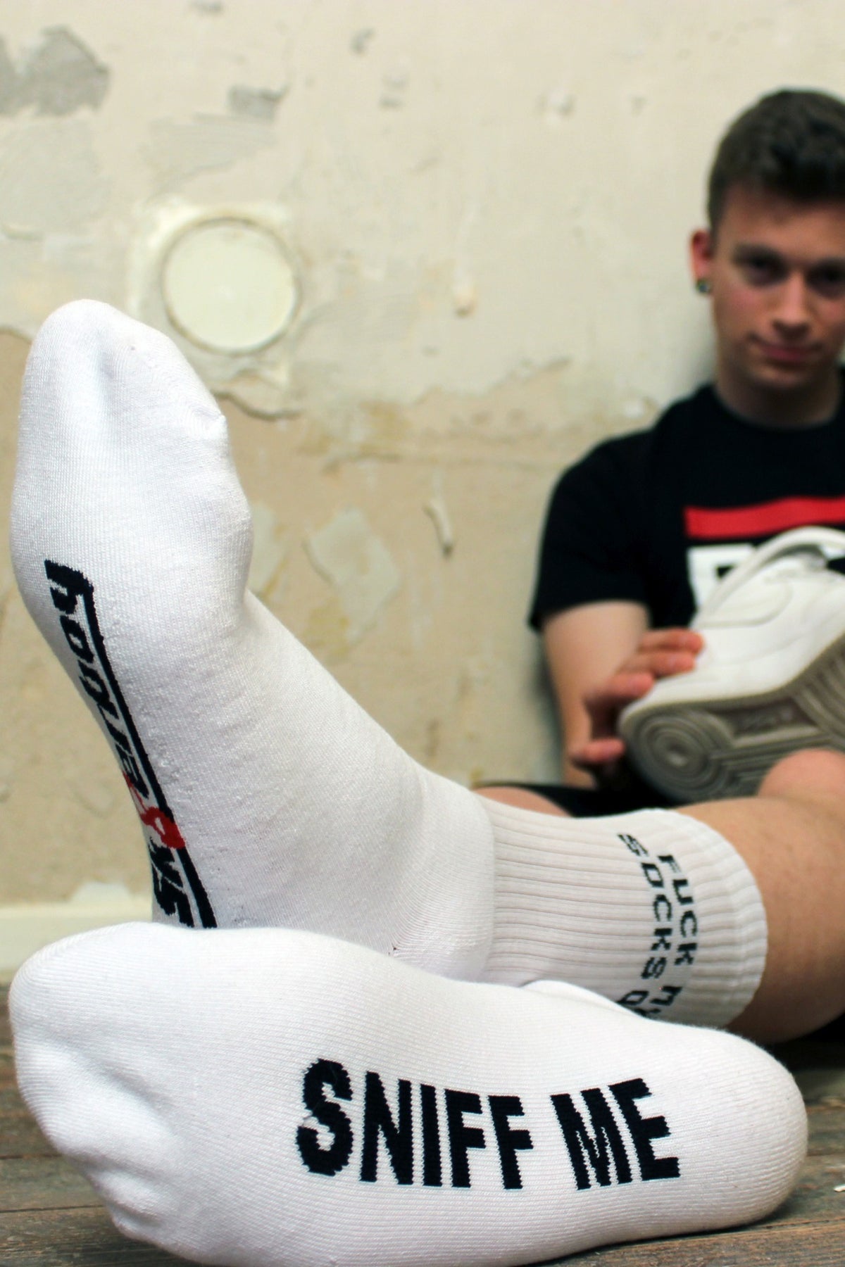 sk8erboy sniff me socks with a bold black print on the white socks, wearing a fck abl T-shirt by sk8erboy, sitting on the floor