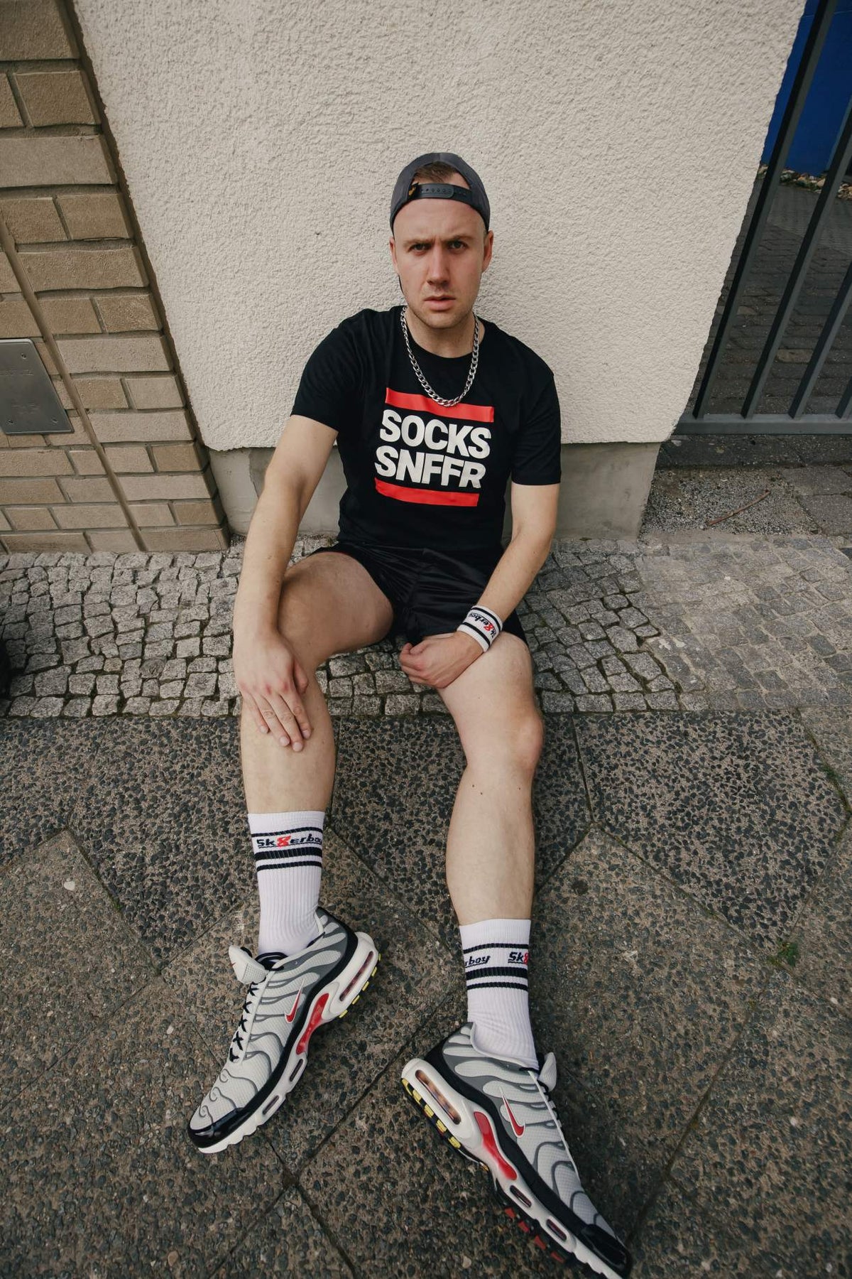 chaussettes sk8erboy Victory extra fines, de qualité reconnue, particulièrement légères et idéales pour l’été, blanches, portées par un jeune homme gay assis au sol avec des baskets Nike TN