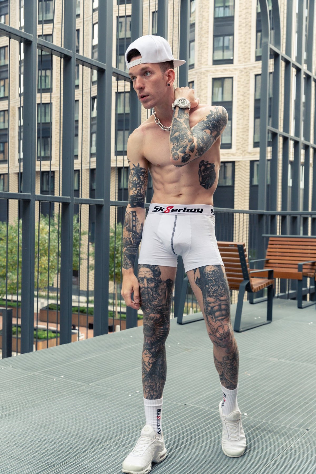 athletic boy shows off his six-pack and bare torso in the city, with tattoos on his legs and arms, wearing white boxer shorts by sk8erboy and matching crew socks with Nike TN sneakers