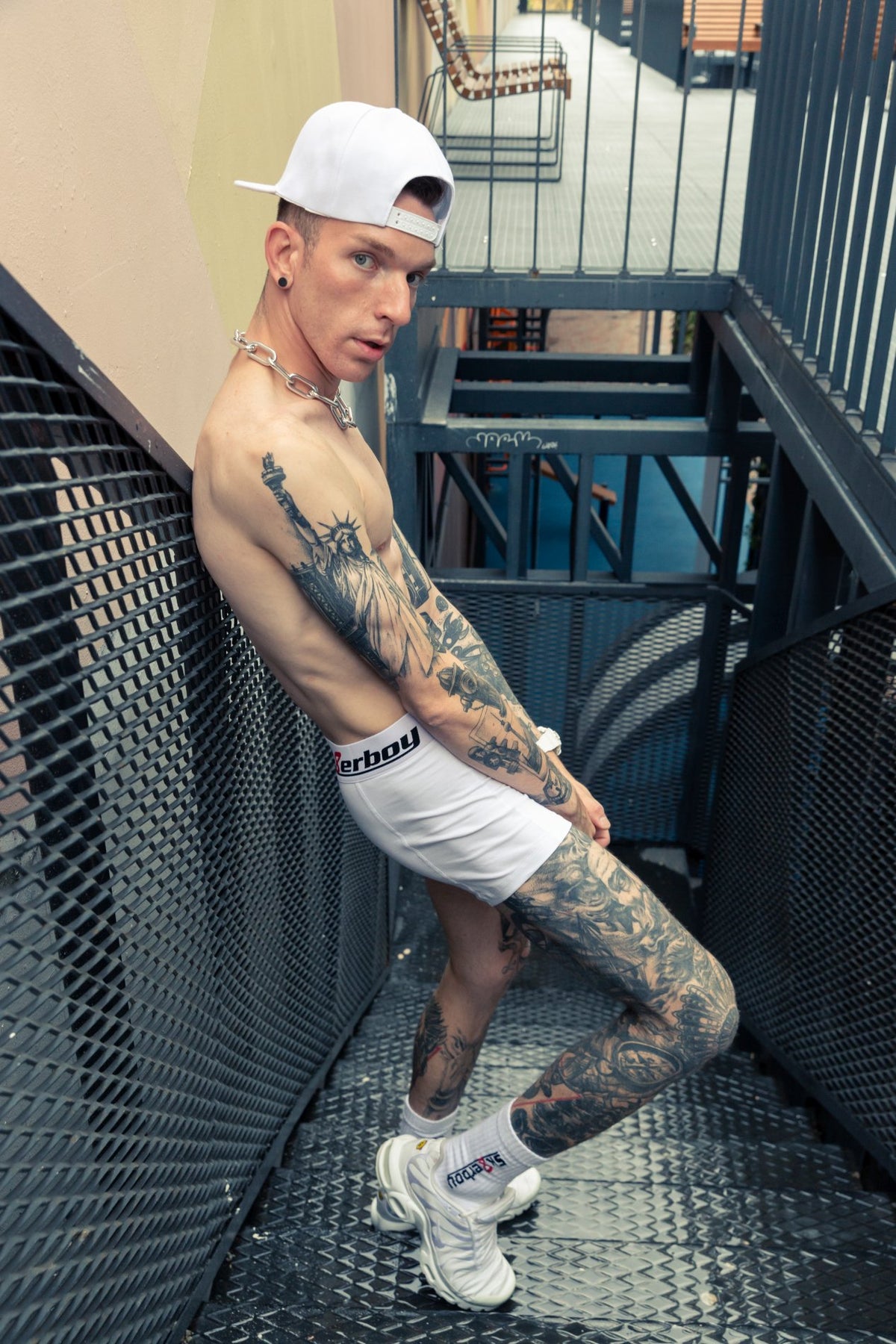 Athletic man on a staircase with a bare, muscular upper body wearing white boxer shorts and crew socks from sk8erboy, with a white cap and Nike TN sneakers