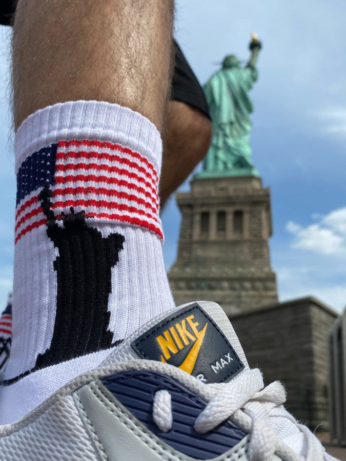USA flagge auf weissen socken vor der freiheitsstatue in new york von einem sportlichen jungen getragen mit nike airmax turnschuhen bei sonnenschein in nahaufnahme