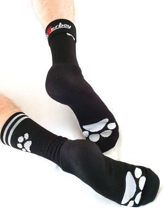 zwei füße mit schwarzen sk8erboy puppy socken mit weißer pfote an der seite und auf der sohle abgebildet mit verstecktem sk8erboy-logo auf der innenseite am bund