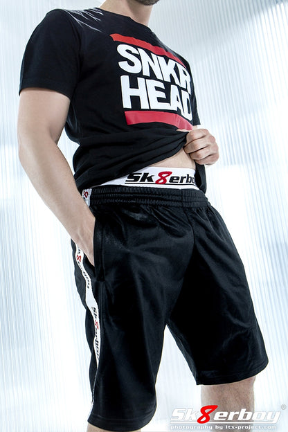 junge mit glanz short von sk8erboy und passender boxershort traegt ein schwarzes snekr sneaker head t-shirt mit weissem aufdruck und roten balken