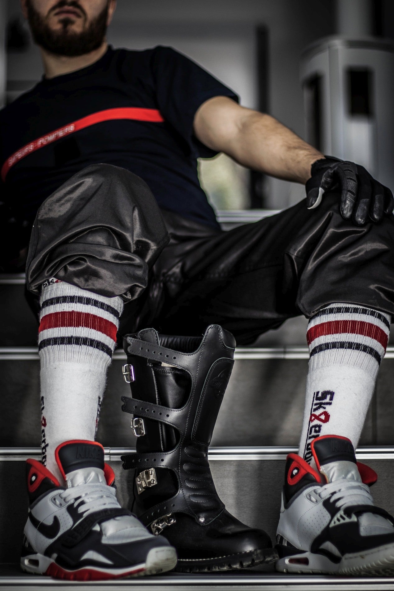 sporty gay mit handschuhen aus leder sitzt in tracksuite auf der treppe und traegt in seinen nike sneaker sk8erboy tubesocks in schwarz weiss rot mit streifen und grossem logo