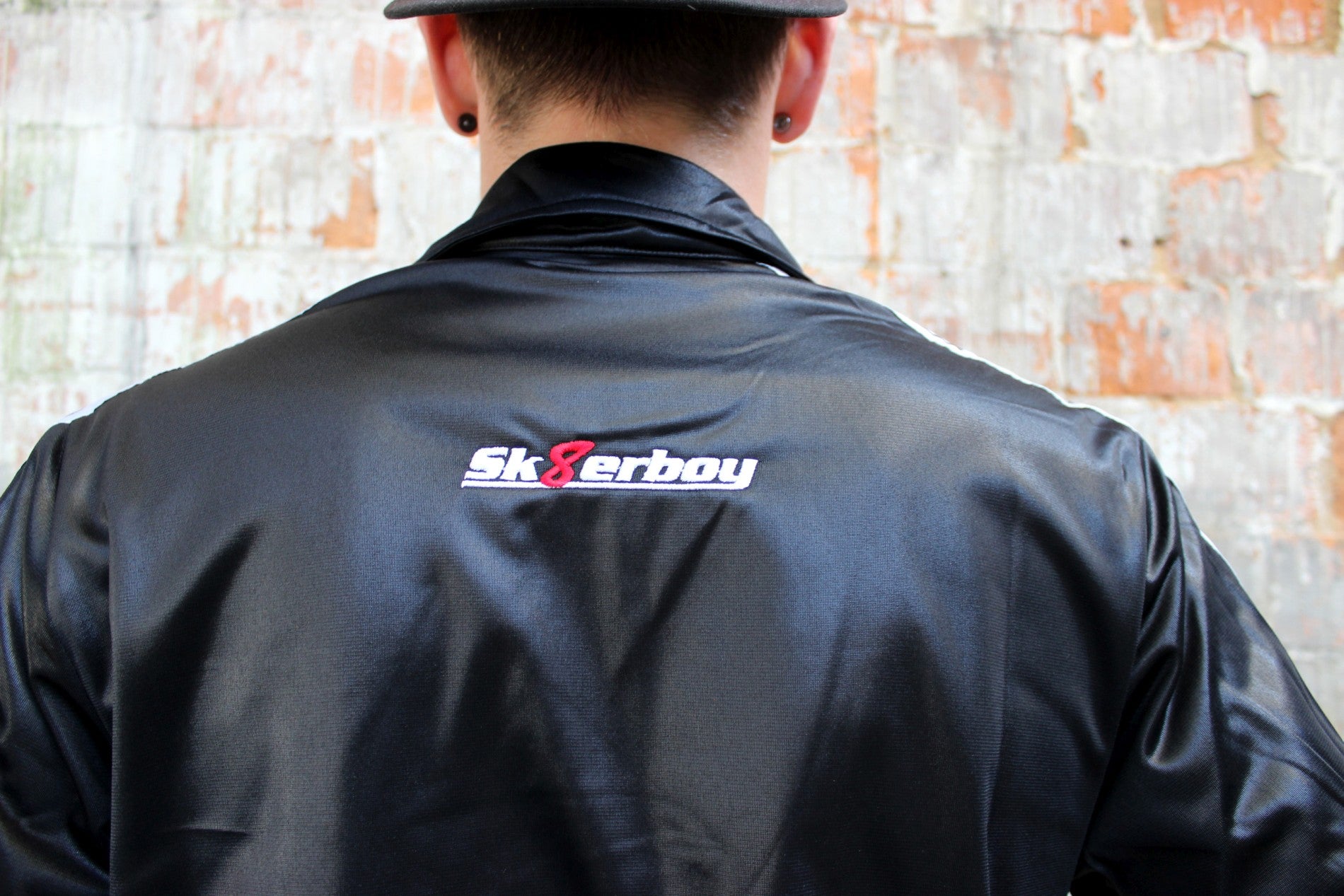 schulter und ruecken der shiny jacket trainingsjacke von sk8erboy in schwarz mit logo zwischen den schultern und schwarzer nike kappe dazu