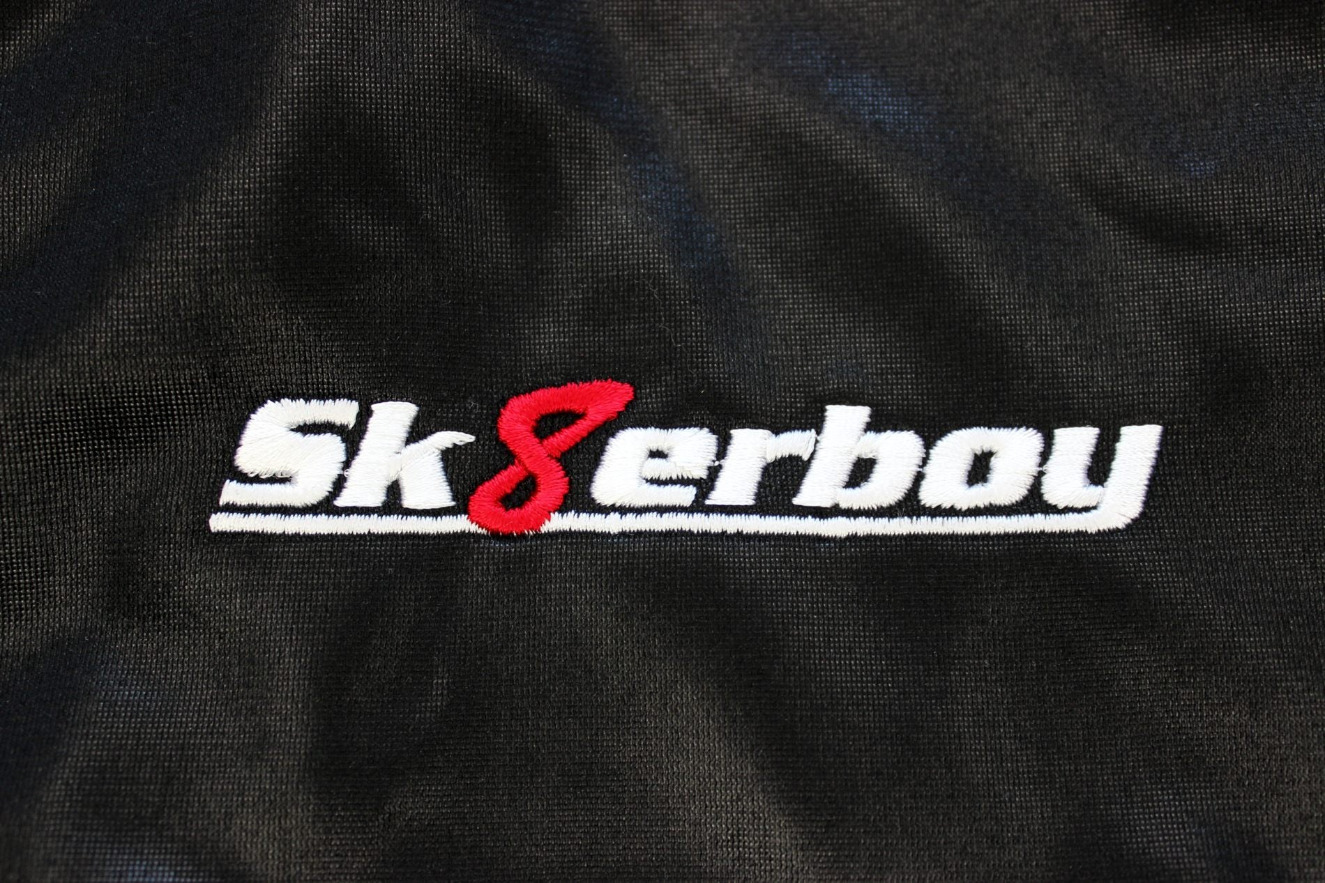 nahaufnahme des eingestickten sk8erboy logo auf der shiny glanz jacke in schwarz mit weisser schrift und roter acht