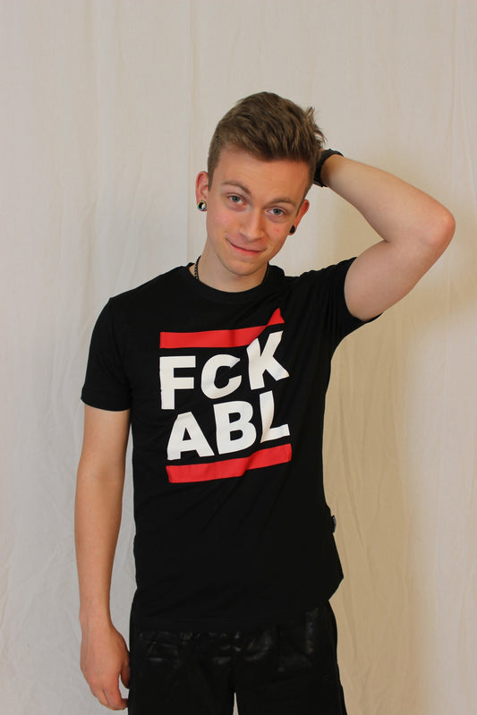 junger gay vor einer wand mit einem schwarzen t-shirt und dem aufdruck fck abl in weiss und zwei roten blaken